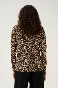 T-shirt à manches longues en imprimé léopard, avec un fond beige et des taches marron foncé, texture douce, silhouette ajustée et col rond.