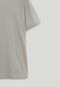 T-shirt gris clair, en coton doux, avec une coupe décontractée, des manches courtes et un col rond. Texture lisse, détails minimaux.