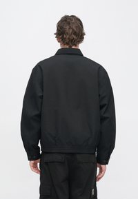 Μαύρο μπουφάν τύπου bomber με γιακά, ελαστικό τελείωμα και μανσέτες, απαλό υλικό και διακοσμητικά κουμπιά στους καρπούς.