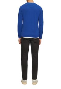 Pull en tricot bleu avec un col rond, des manches longues et des poignets côtelés, associé à un jean sombre et des baskets de couleur claire.