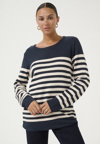 Jūras spēku un krējuma svītrains puloveris ar brīvu piegriezumu, apaļu kakla izgriezumu un garām piedurknēm, ar ribotas aproces un apakšmalu.