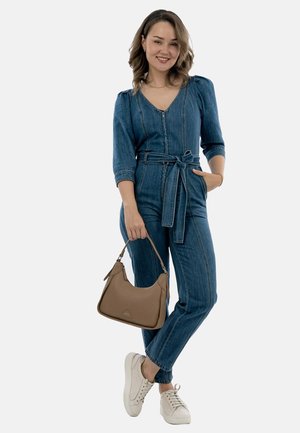 Denim overall in medium blauw met een getailleerde taille, driekwart mouwen en een rits. In combinatie met een bruine handtas en witte sneakers.
