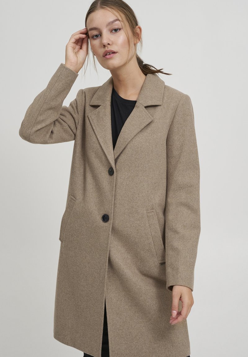 Cappotto beige in misto lana con colletto a rever, due tasche frontali e bottoni neri. Vestibilità tailored con silhouette dritta e dettagli minimi.