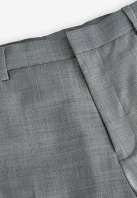 Pantalones grises a medida confeccionados con tejido texturizado. Cuentan con una cinturilla plana y un pliegue delantero limpio, exhibiendo un sutil patrón tejido.