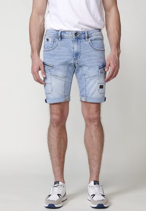 Lichtblauwe denimshorts met opgerolde pijpen, cargozakken aan de zijkanten en een gestructureerde afwerking. Draag met witte sportschoenen.