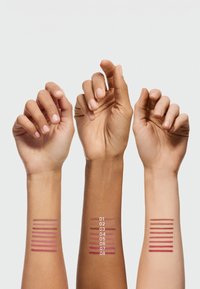 Trois bras présentent des échantillons de couleurs de rouge à lèvres dans différentes nuances sur la peau. Les étiquettes 01-08 sont visibles à côté des échantillons. Texture lisse.