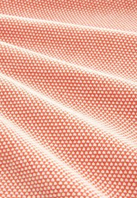 Gros plan sur un tissu texturé avec de petits points orange et blancs, espacés de manière régulière, créant un motif en forme de gaufre.