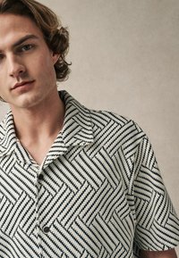 Camisa de manga corta con un patrón en zigzag en blanco y negro, fabricada con un tejido texturizado, con un cuello con muesca y cierre de botones.