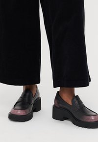 Svarte skinnloafers med en tykk hæl, med en gradient lilla aksent ved tåen og teksturerte såler.