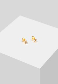 Guld hjärtformade stiftörhängen med tre små klara ädelstenar i mitten, med en polerad yta och en mjuk textur.
