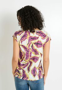 Túnica de manga corta en una tela ligera, con un patrón de hojas multicolores en púrpura, amarillo y blanco, con un corte holgado y un dobladillo redondeado.