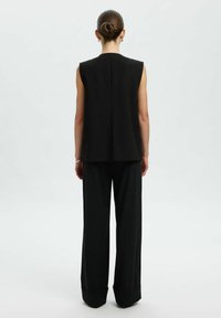Schwarzes ärmelloses Top mit geradem Schnitt und einer Rückennaht, kombiniert mit locker sitzenden schwarzen Hosen. Minimalistisches Design und glatte Stoffoberfläche.