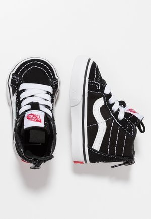 Een paar zwart-witte baby Vans sneakers met witte veters en rood logo op een witte achtergrond.