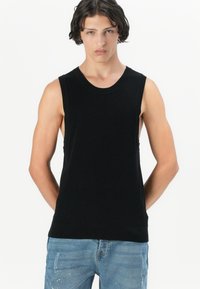 Juodas raštuotas tank top'as su apvaliu kaklu ir be rankovių dizainu, derinamas su šviesiai mėlynomis nusidėvėjusiomis džinsomis. Lygi tekstūra, prigludusi forma.