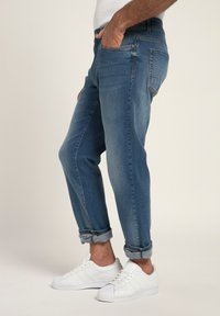 Jeans de mezclilla azul con un corte relajado, puños doblados y un diseño clásico de cinco bolsillos, combinados con zapatillas blancas.