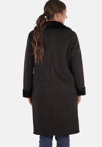 Cappotto lungo nero realizzato in morbido tessuto, con colletto e polsini in pelliccia sintetica, dal taglio dritto e con dettagli delle cuciture visibili sul retro.