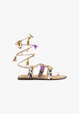 Platte sandaal met meerkleurige kwastjes en decoratieve kralen. Gemaakt met lerenachtige banden, versierd met stippen en kralenaccenten.