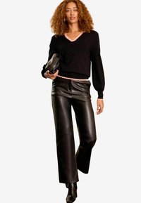 Svart tröja med rosa scallopkant och manschetter, i kombination med högmidjade svarta läderbyxor. Accessoar: svart clutch. Minimalistisk outfitdesign.