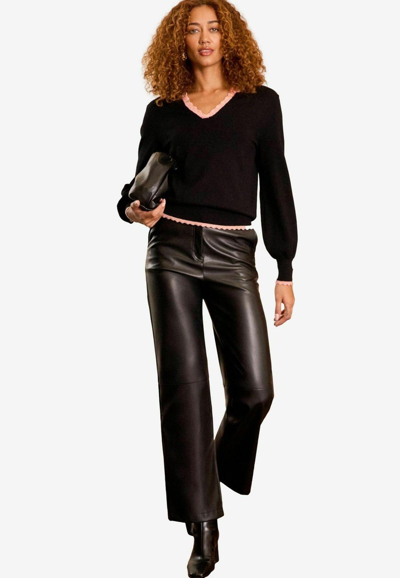 Svart tröja med rosa scallopkant och manschetter, i kombination med högmidjade svarta läderbyxor. Accessoar: svart clutch. Minimalistisk outfitdesign.