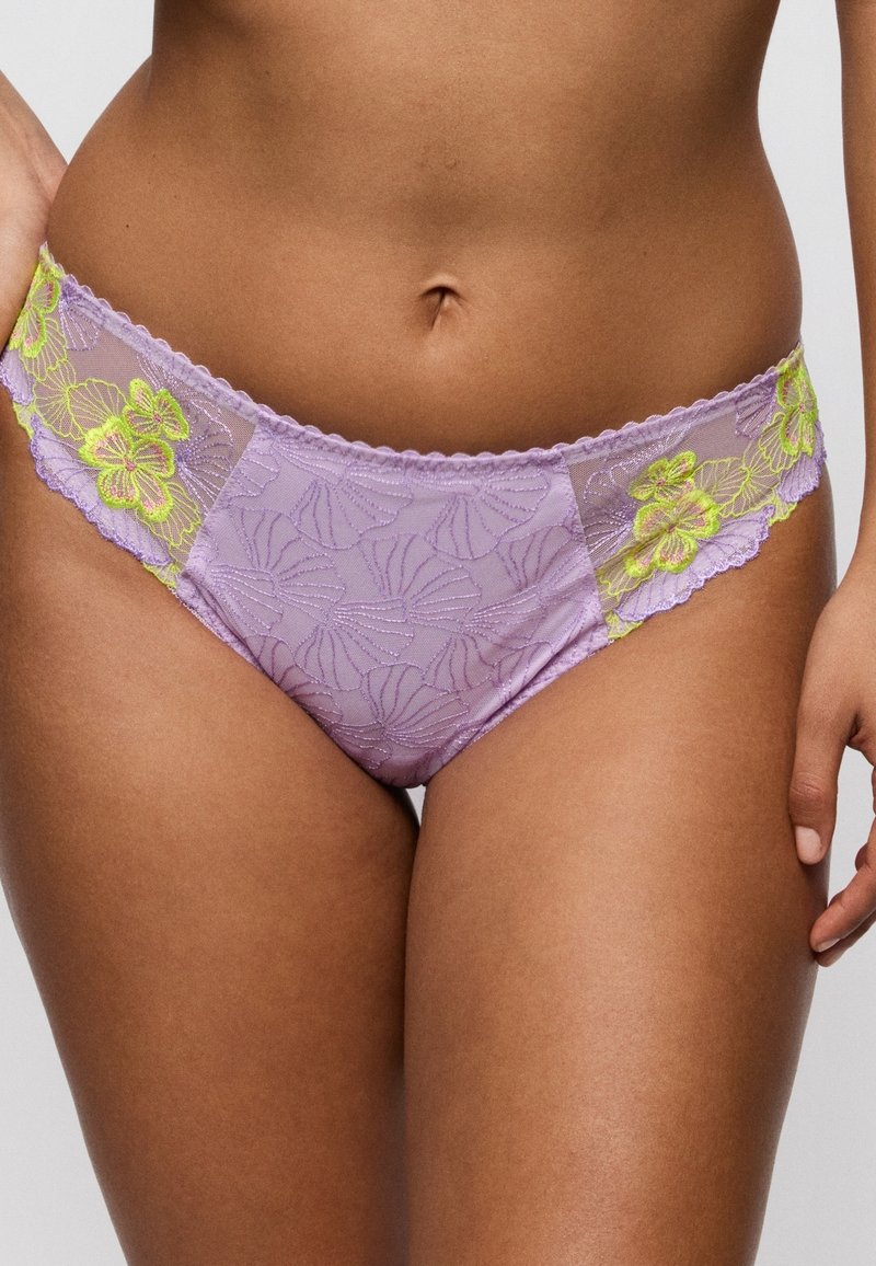 Fioletowa koronkowa bielizna z żółtym, kwiatowym haftem noszona przez osobę, ukazująca środkową część ciała i górne części ud na jednolitym tle.