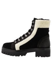 Botas de tobillo de ante negro con ribete de borreguito blanco, accesorios de acero inoxidable y suela negra resistente. Cuenta con un diseño de cordones con ojales reforzados.