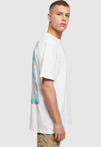 Hvid bomulds t-shirt med løs pasform, der har et flerfarvet grafisk design i pastelnuancer på ryggen.
