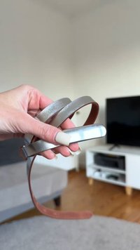 Three hairbands in hand: one metallic silver with a smooth texture and two brown leather with a matte finish, showcasing varying widths.