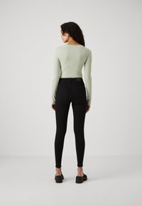 Light green ribbed long-sleeve top paired with high-waisted black skinny jeans. Black platform sandals complete the outfit. Back view shown.