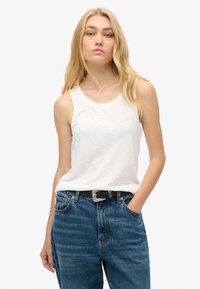 Witte mouwloze tanktop met een ronde halslijn, gecombineerd met hoogwaisted blauwe jeans en een zwarte riem met een zilveren gesp.