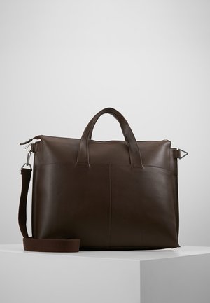 Dunkelbraune Leder-Aktentasche mit zwei kurzen Griffen und einem abnehmbaren Schultergurt auf einem weißen Podest.