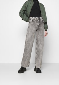 Grön quiltad bomberjacka, svart ribbad polokrage och grå vida jeans med en sliten finish. Svarta platåstövlar.