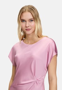 Satin-Pinkes Oberteil mit kurzen Ärmeln, das über ein gedrehte Detail an der Taille für zusätzlichen Textur verfügt. Glatte Oberfläche und lockere Passform.