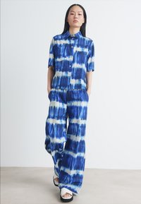Ensemble assorti en tie-dye bleu comprenant une chemise à col à manches courtes et un pantalon ample avec une taille élastique. Texture de tissu lisse.