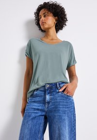 T-shirt vert clair à manches retroussées, ample, associé à un jean taille haute en denim bleu clair à jambes évasées avec une finition décolorée.