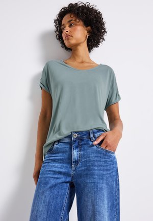 Lyst grøn, løs pasform t-shirt med oprullede ærmer, parret med højtaljede lysblå vide jeans med en falmet finish.