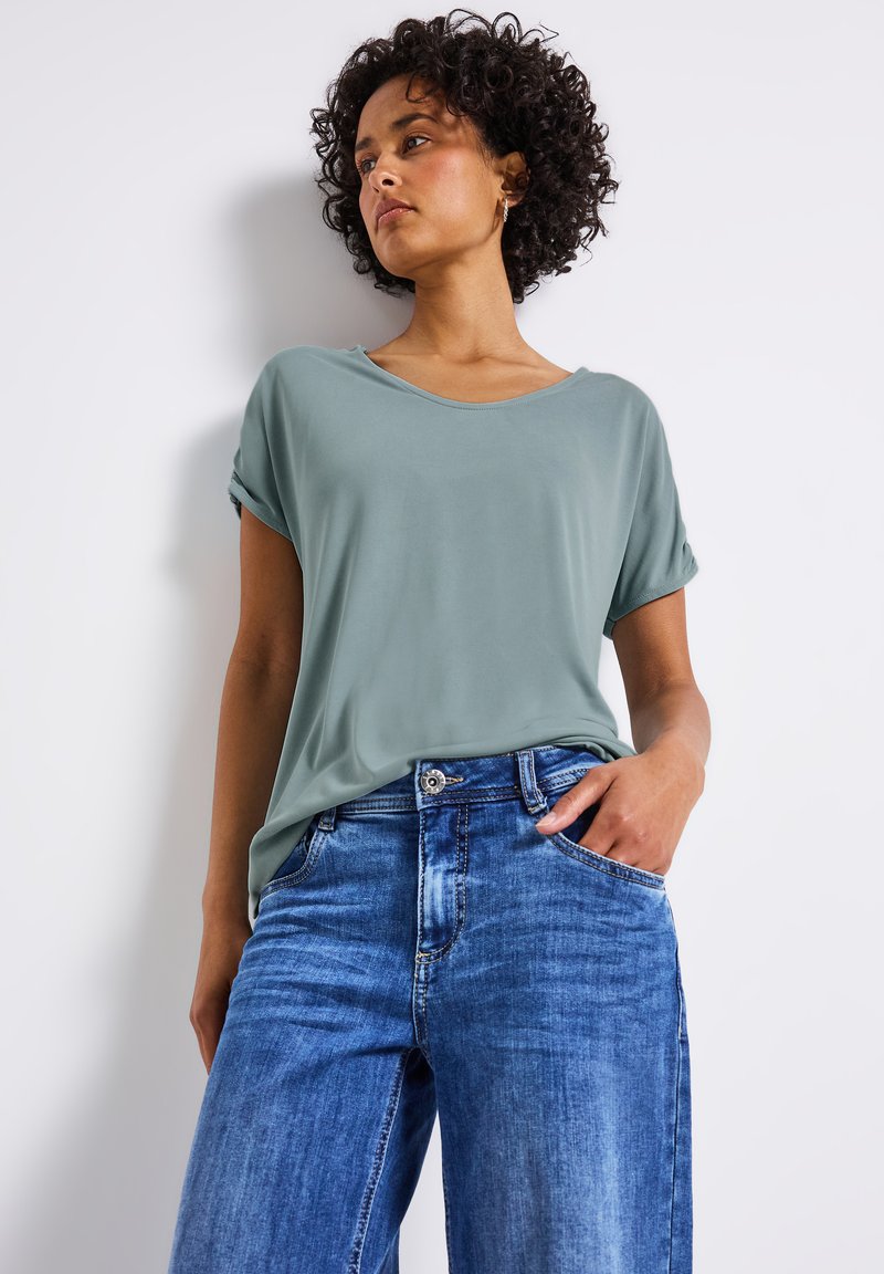 T-shirt vert clair à manches retroussées, ample, associé à un jean taille haute en denim bleu clair à jambes évasées avec une finition décolorée.
