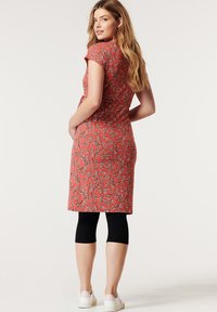 Vestido floral vermelho com mangas curtas, silhueta ajustada e comprimento até ao joelho, usado sobre leggings pretas e sapatilhas brancas.