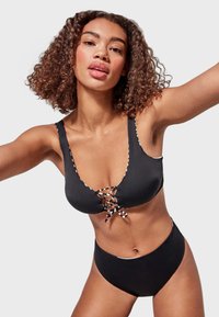 Conjunto de bikini negro que presenta un top de escote pronunciado con detalles de cordones y ribetes en contraste, combinado con unas braguitas de cintura alta. Textura suave.