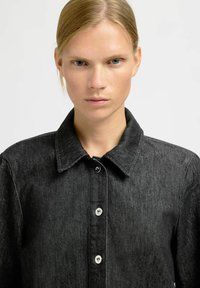 Black denim shirt with a collar, single-breasted buttons, and a textured fabric. Features a subtle herringbone pattern.