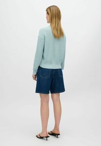 Light blue knitted sweater with dropped shoulders, paired with dark blue denim shorts. Model wearing black heeled sandals.