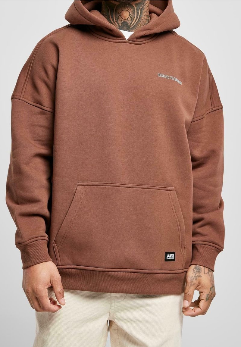 Sudadera marrón con un bolsillo frontal, capucha y puños acanalados. Presenta un bordado de logo mínimo. Tejido suave con una textura lisa.