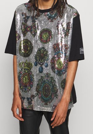 Czarny t-shirt z krótkim rękawem z przodem pokrytym srebrnymi cekinami, zdobionym kolorowymi, ozdobnymi wzorami, ułożonymi w różnorodne kształty i desenie.