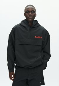 Čierna, ľahká pulóverová bunda s kapucňou, polozipsom, predným vreckom a červeným nápisom loga "Double V" na hrudi. Má elastické manžety.