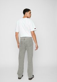 Lichtgrijze denim jeans met een rechte pijp en achterzakken, gecombineerd met een wit T-shirt met een klein logo op de mouw.