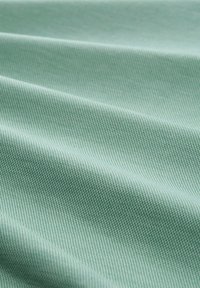 Světlé zelené tkaniny s texturovanou vazbou vykazuje jemné diagonální čáry a vrásky, které ukazují hladký, jemný povrch.