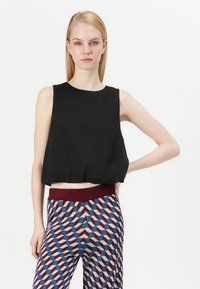 Top corto nero con scollo rotondo, abbinato a pantaloni con motivo a geometrie nei colori rosso, blu e crema. Tessuto liscio.