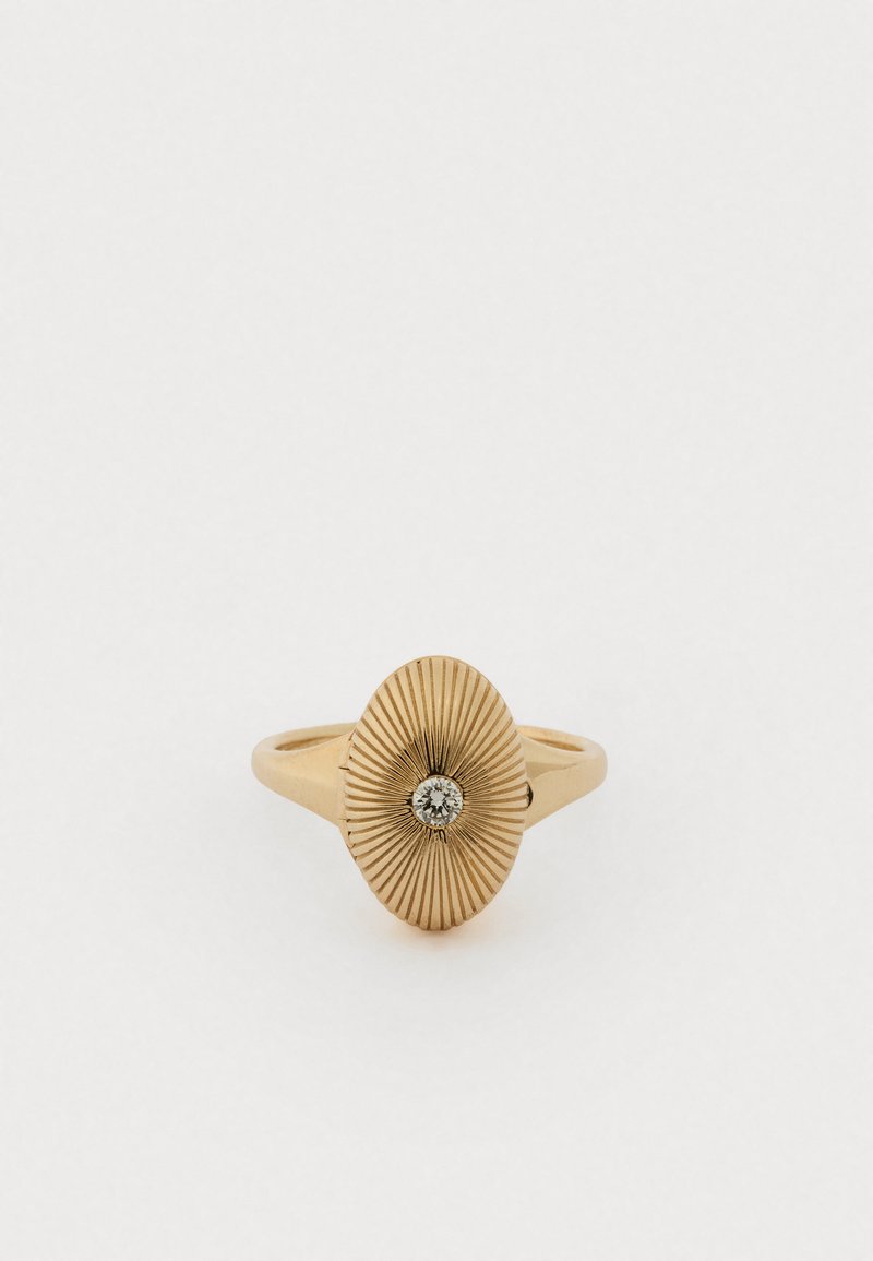 Gold ring with an oval-shaped, textured design featuring radiating lines, centered diamond accent. Smooth band.