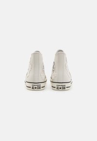 HVIDE HØJTOP SNEAKERS MED SKYFORMEDE DETALJER, SORTE LOGO-PATCHES OG STRIBET GUMMISÅL. HAR TEXTURERET LÆDEROVERDEL OG SNØRRELSLUTNING.