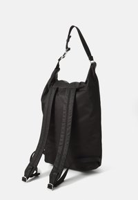 Zwarte rugzak van nylon, met verstelbare schouderbanden, een handvat bovenop, en een textuurpanelenontwerp met een minimalistische silhoutte.
