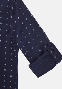 Manica di camicia blu navy con motivo a pois bianchi e rossi, caratterizzata da un design con bottone e risvolto. Tessuto liscio con forma strutturata.